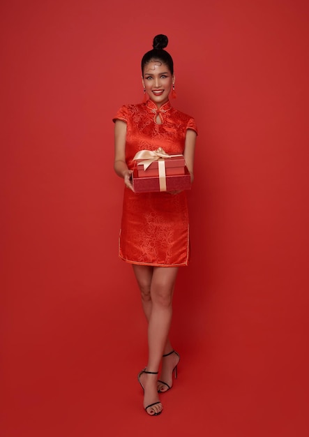 Feliz mujer asiática sonriente vestida con traje tradicional rojo dando caja de regalo para bendecir el año nuevo chino
