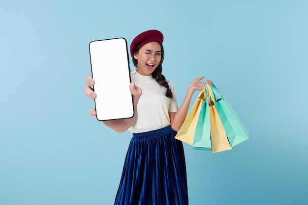 Foto gratuita feliz mujer asiática tailandesa disfrutando de las compras, lleva bolsas de compras y muestra el teléfono móvil