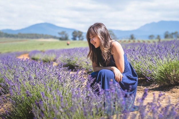 Feliz mujer asiática en un vestido largo azul posando en el campo de lavanda