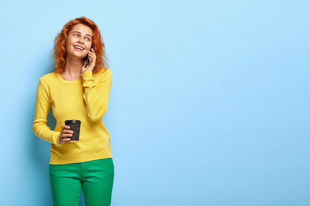 Feliz mujer astuta de ojos azules llama novio en el teléfono móvil, expresa emociones positivas