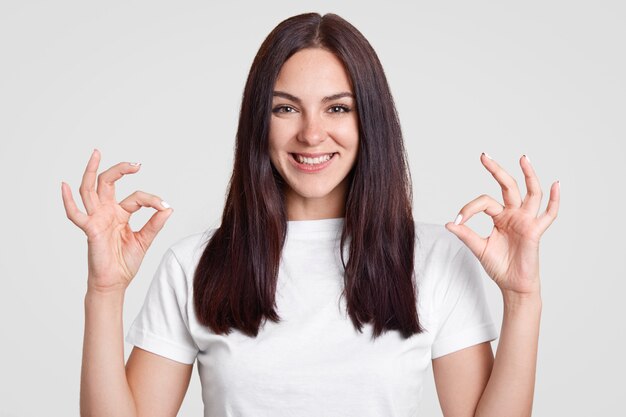 Feliz mujer atractiva con cabello largo y liso y oscuro, hace un buen signo con ambas manos, muestra aprobación