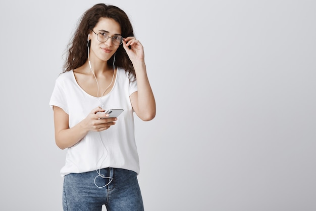 Feliz mujer atractiva mediante teléfono móvil, escuchando música en auriculares