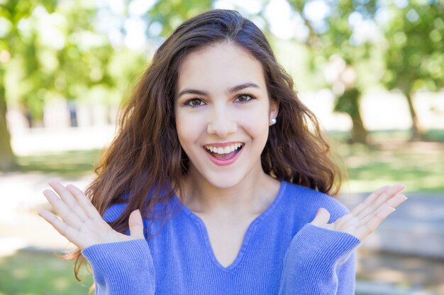 Feliz mujer bastante joven levantando las manos en el parque