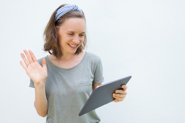 Feliz mujer bastante joven con tableta saludando hola en pantalla