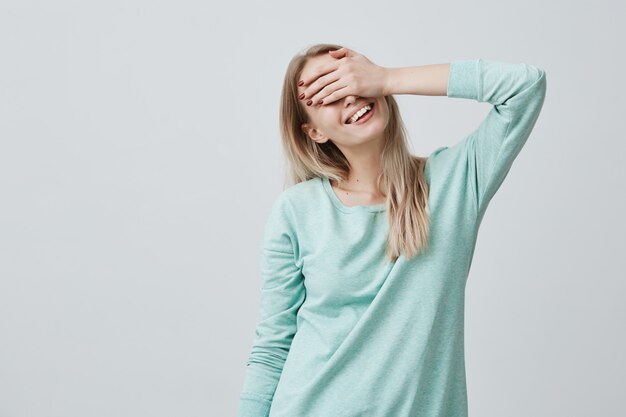 Feliz mujer con cabello rubio cerrando los ojos con la mano