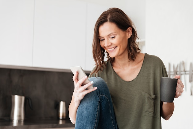 Feliz mujer casual con smartphone y tomando café en casa