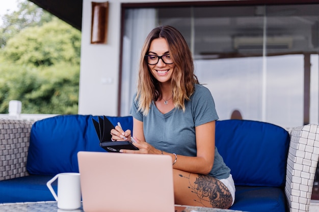 Feliz mujer caucásica hace trabajo a distancia en el portátil en casa lugar cómodo bebiendo té