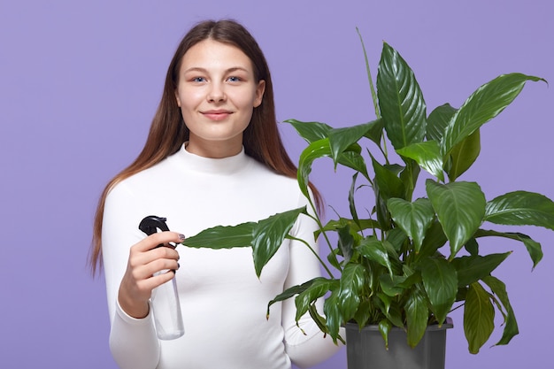 Feliz mujer caucásica o ama de casa rociando planta de interior con rociador de agua en casa