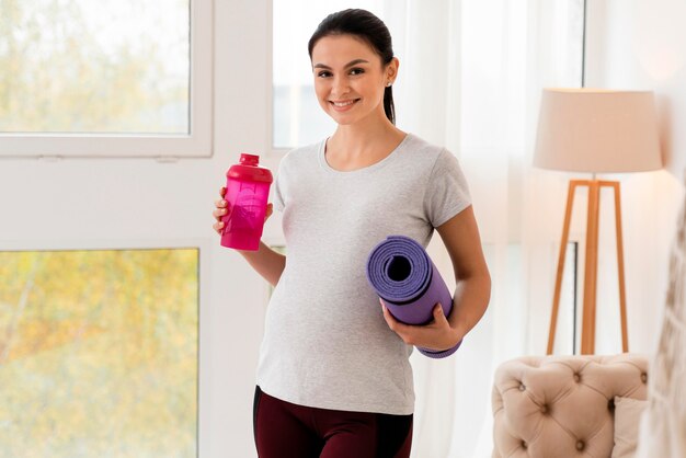 Feliz mujer embarazada sosteniendo una colchoneta de fitness y una botella de agua