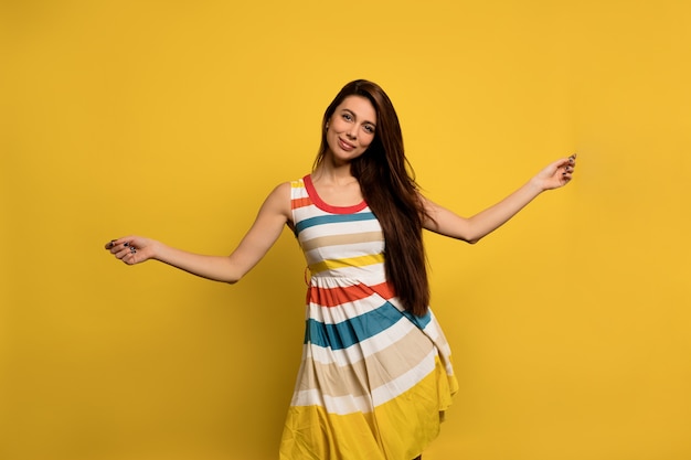 Feliz mujer emocionada con cabello largo oscuro en vestido de verano a rayas brillantes se divierte y baila Emociones felices de la mujer europea.