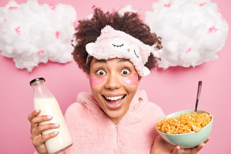 Foto gratuito feliz mujer étnica sorprendida con cabello afro mira con alegría a la cámara sostiene un tazón de cereales con leche viste ropa de dormir te mira positivamente disfruta de un desayuno saludable y procedimientos de belleza