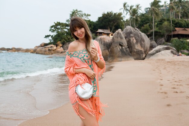 Feliz mujer europea con pelos largos en elegante vestido de verano boho posando en la playa tropical.