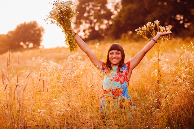 Foto gratuita feliz mujer con flores se encuentra en el campo de la tarde