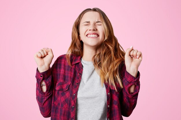 Foto gratuita feliz mujer ganadora con una sonrisa agradable, aprieta los puños y los dientes, alegra su victoria o logro gran éxito