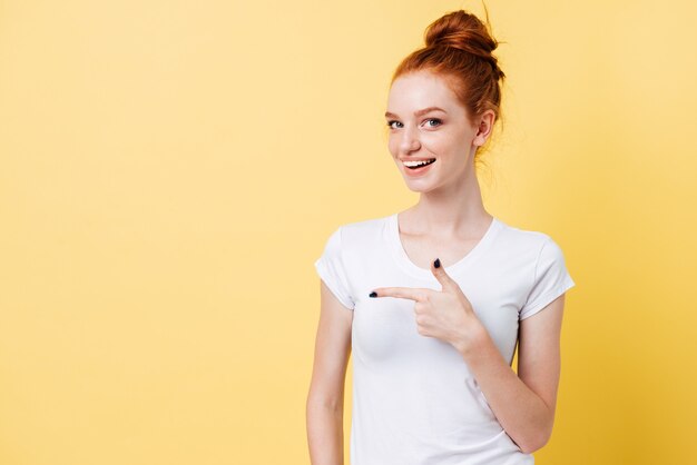 Feliz mujer de jengibre en camiseta apuntando lejos