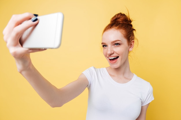 Feliz mujer de jengibre en camiseta haciendo selfie en su teléfono inteligente