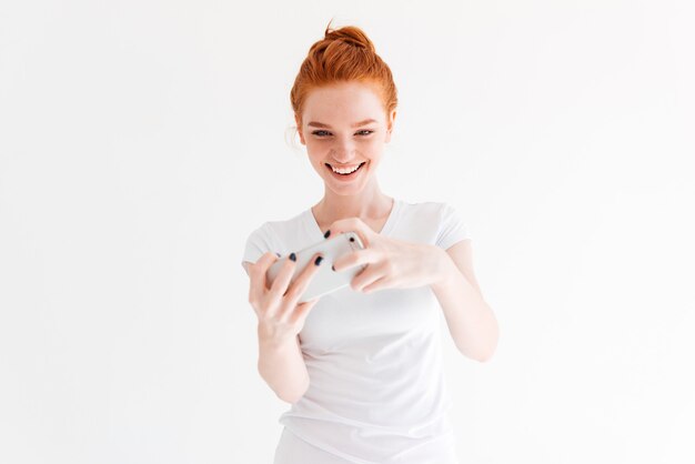 Feliz mujer de jengibre en camiseta jugando en su teléfono inteligente