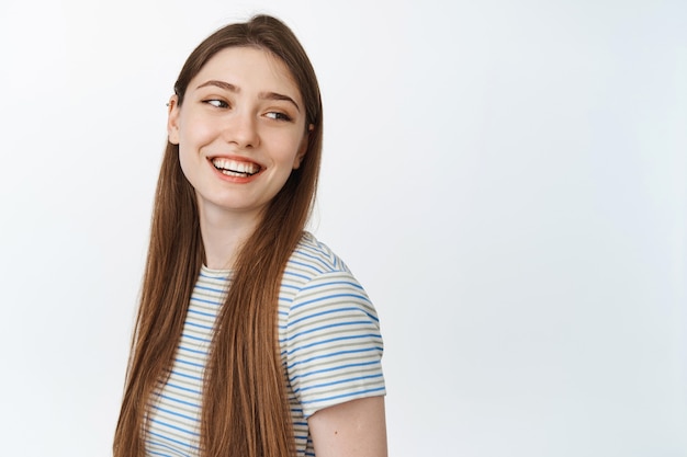 Feliz mujer joven con cabello largo natural, mirando a un lado el espacio vacío para pancarta y sonriendo, riendo alegre en blanco