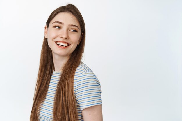 Feliz mujer joven con cabello largo natural, mirando a un lado el espacio vacío para pancarta y sonriendo, riendo alegre en blanco