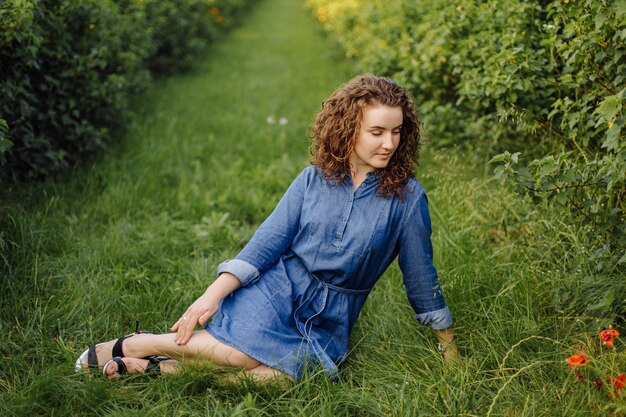 Feliz mujer joven con cabello rizado castaño, vestido, posando al aire libre en un jardín