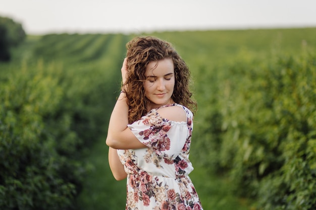 Feliz mujer joven con cabello rizado castaño, vestido, posando al aire libre en un jardín