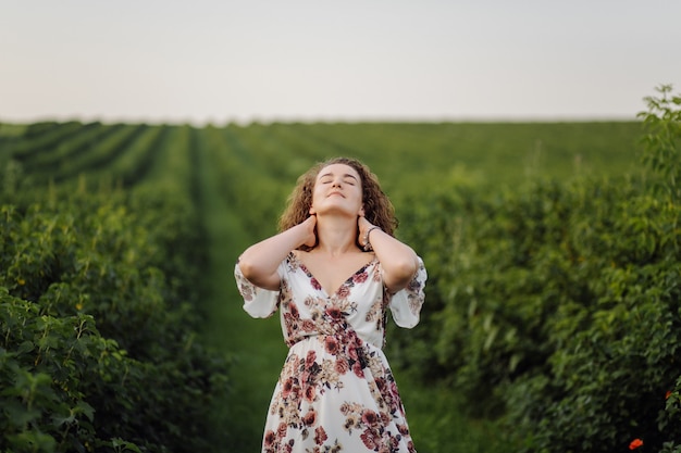 Feliz mujer joven con cabello rizado castaño, vestido, posando al aire libre en un jardín