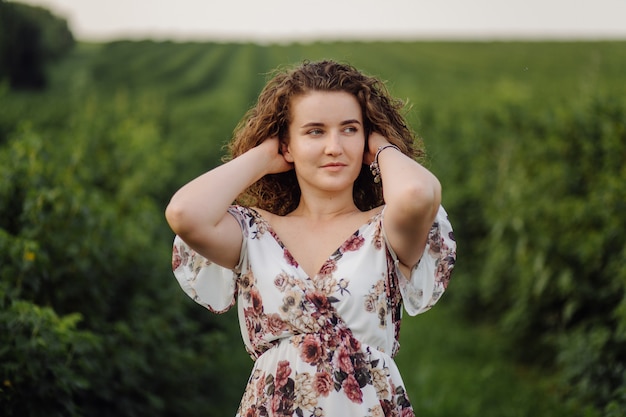 Feliz mujer joven con cabello rizado castaño, vestido, posando al aire libre en un jardín