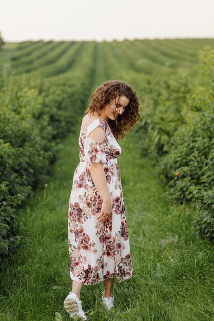 Feliz mujer joven con cabello rizado castaño, vestido, posando al aire libre en un jardín