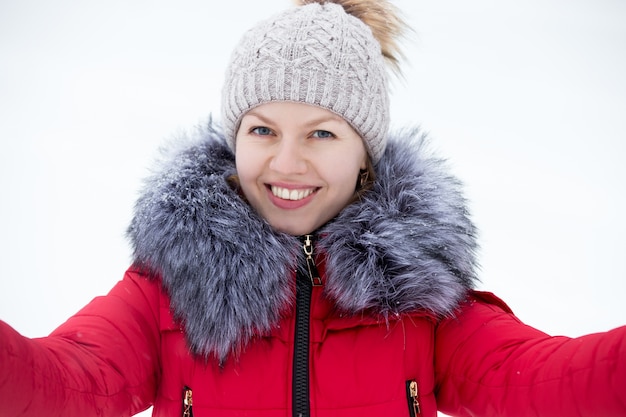 Feliz mujer joven en chaqueta de invierno rojo teniendo auto-retrato, al aire libre contra la nieve