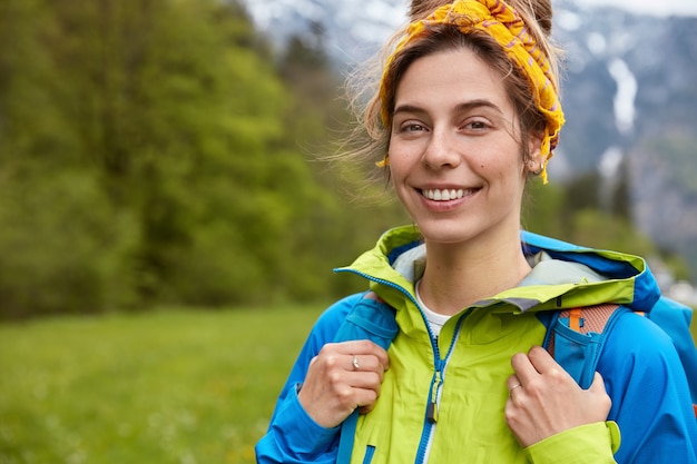 Feliz mujer joven despreocupada posa en la colina de la montaña, sonríe a la cámara