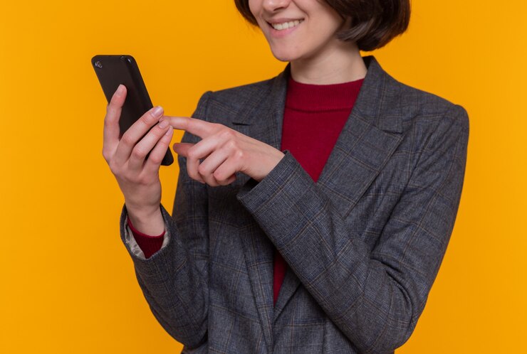 Foto gratuito feliz mujer joven con pelo corto vistiendo chaqueta gris con smartphone