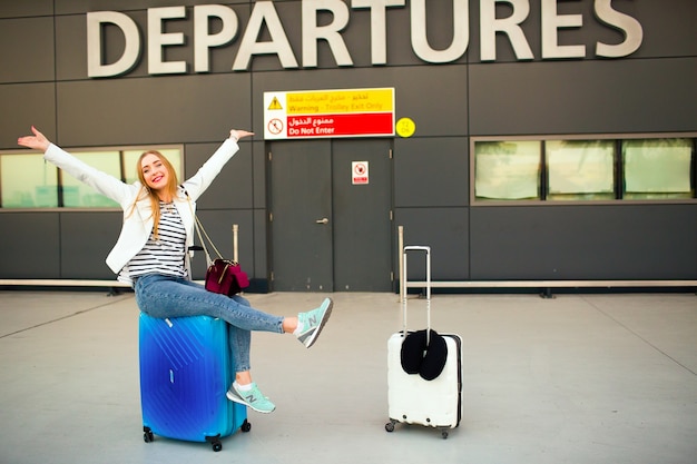 Foto gratuita feliz mujer levanta sus manos sentado en la maleta azul antes