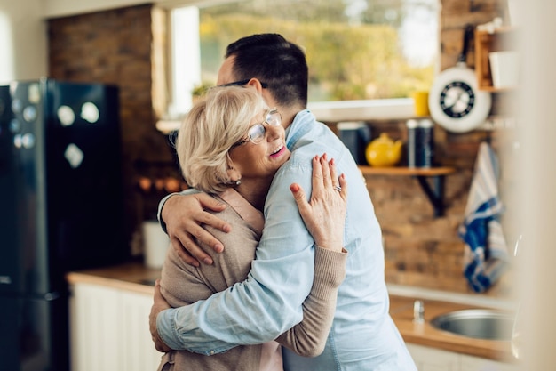 Feliz mujer madura y su hijo adulto abrazándose en la cocina