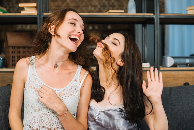 Feliz mujer mirando a su amiga haciendo bigote falso con su pelo