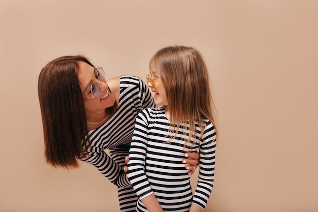 Feliz mujer morena con peinado corto mirando a su encantadora niña sonriente y divertirse sobre fondo aislado