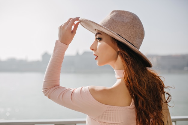 Feliz mujer morena de pelo largo en traje rosa posando en el malecón