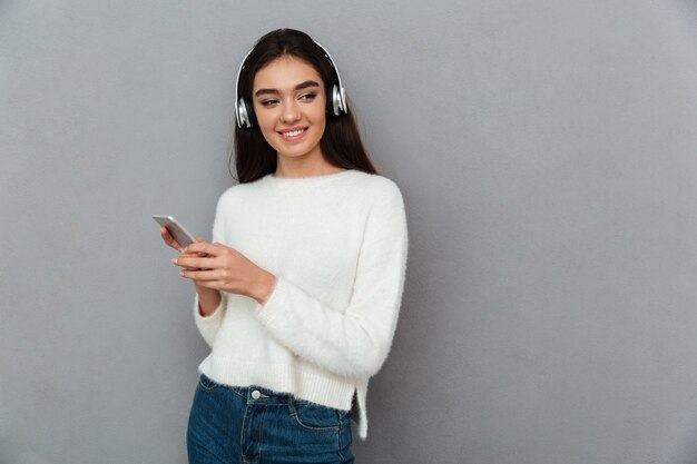 Feliz mujer morena en suéter y auriculares escuchando música