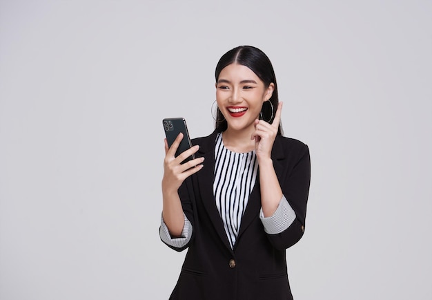 feliz mujer de negocios asiática en traje usando comunicarse teléfono aislado en fondo gris