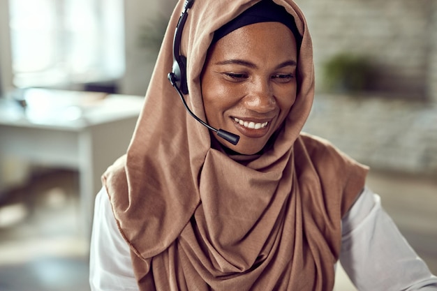 Feliz mujer de negocios islámica con auriculares mientras trabaja en la oficina