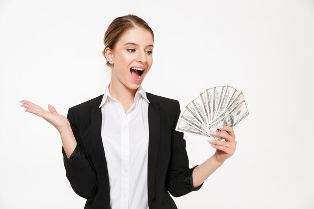 Feliz mujer de negocios rubia gritando con dinero y mirando sobre su pared blanca