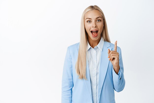 Feliz mujer de negocios en traje apuntando hacia arriba gritando de emoción demostrando el fondo blanco de la pancarta de la empresa de publicidad