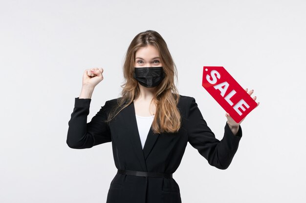 Feliz mujer de negocios en traje con su máscara médica y mostrando la venta en blanco aislado