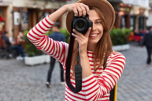 Feliz mujer pasa tiempo libre en hobby, toma fotografías de la calle de la ciudad en la cámara durante el ocio