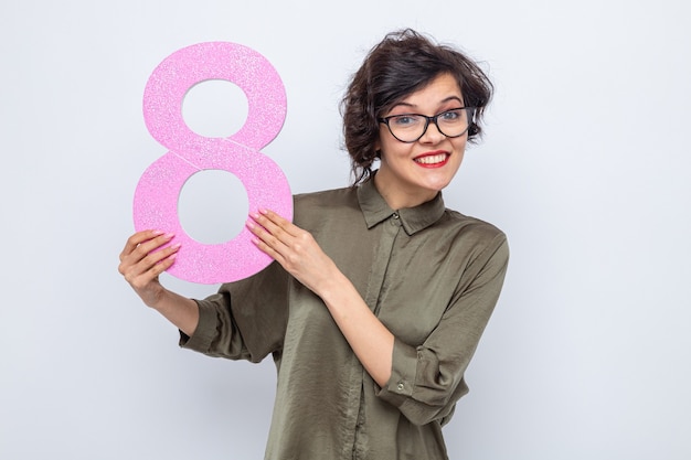 Feliz mujer con pelo corto sosteniendo el número ocho de cartón mirando sonriendo alegremente celebrando el día internacional de la mujer el 8 de marzo