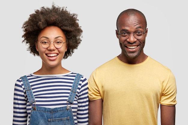 Feliz mujer de piel oscura con peinado afro, se encuentra cerca del chico afroamericano, vestida con una camiseta amarilla informal, aislada sobre una pared blanca. Concepto de personas, etnia y amistad