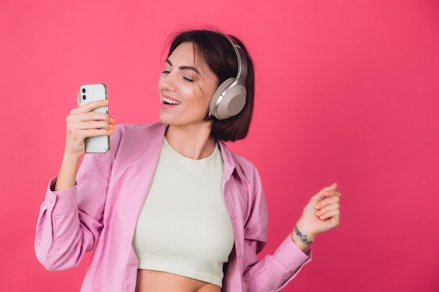 Feliz mujer positiva en auriculares en la pared roja rosa