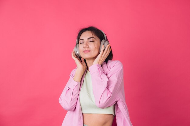 Feliz mujer positiva en auriculares en la pared roja rosa