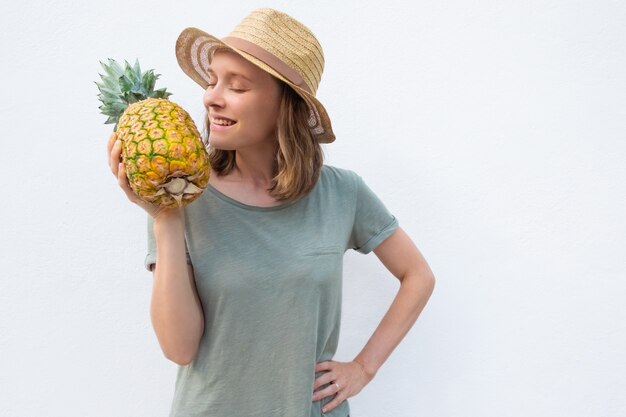 Feliz mujer positiva en sombrero de verano que huele a piña entera