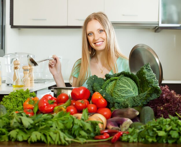 Feliz mujer rubia cocina con montón de verduras