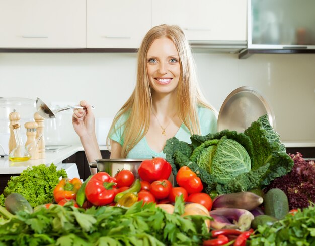 Feliz mujer rubia cocina con verduras en la cocina